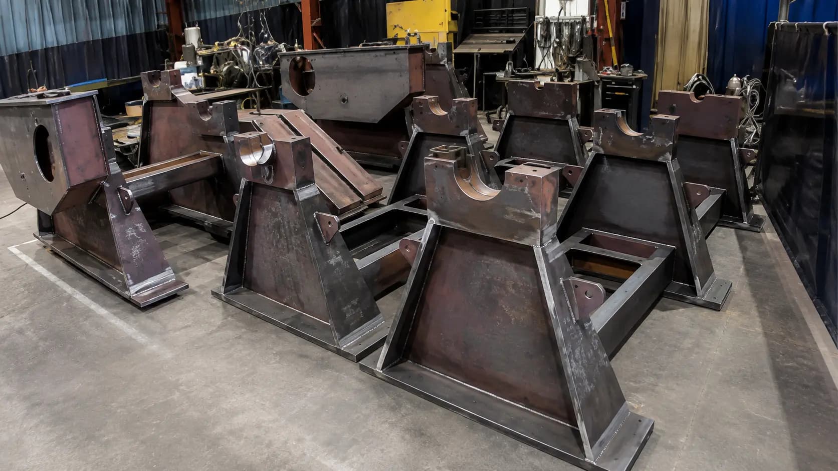 Row of dark fabricated steel weldments staged on the floor